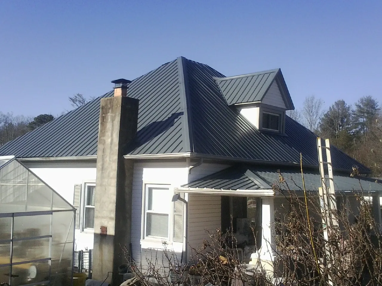 Dark blue standing seam metal roof on a white farmhouse with dormer — Slate & Tile Roof Repair by Roofing Brothers in Rogers