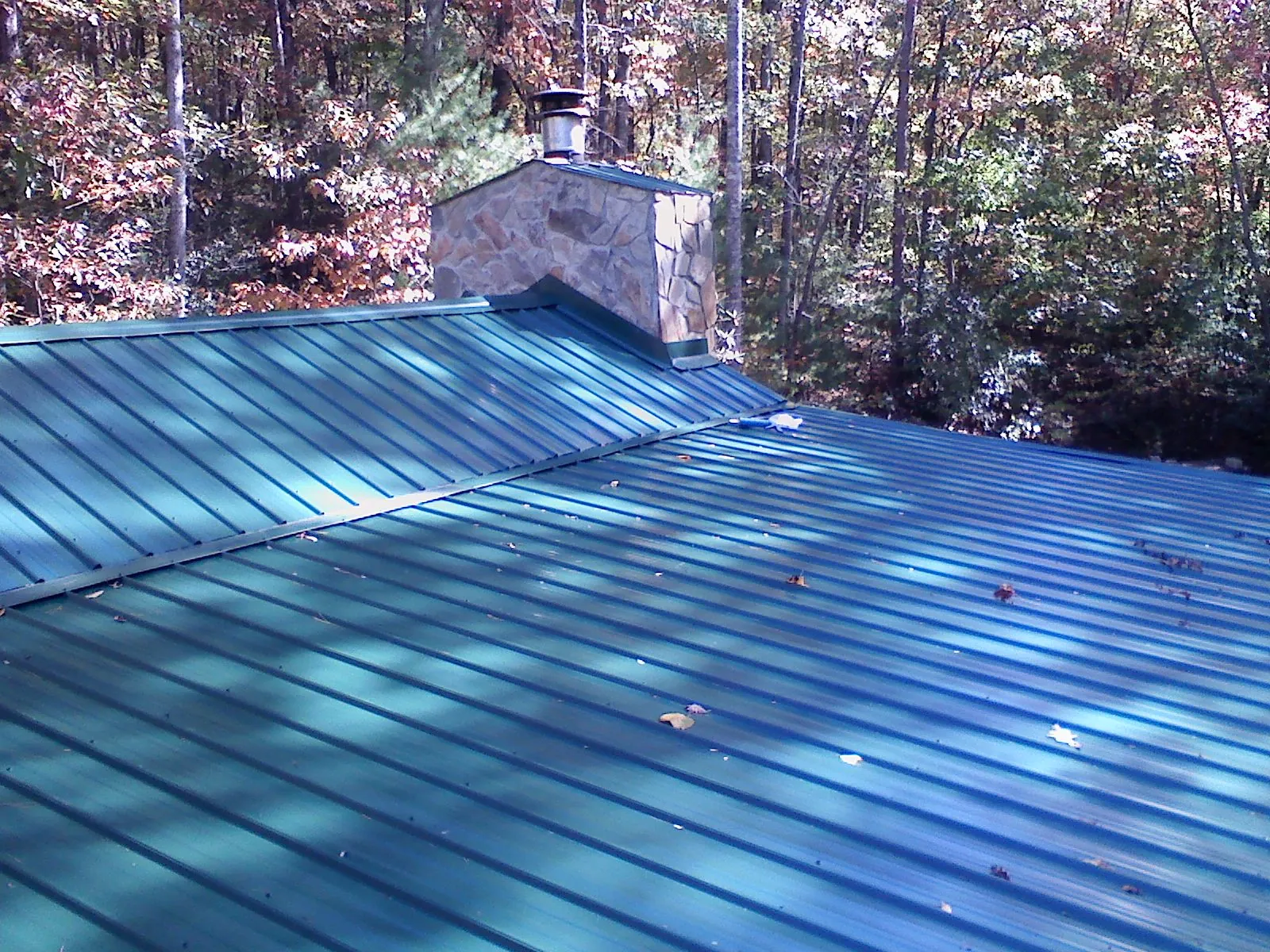 New green metal roof and stone chimney surrounded by autumn woods in Rogers